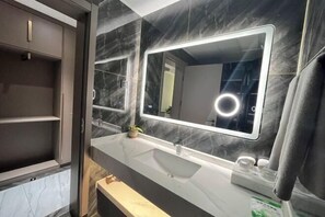 A modern bathroom with a marble vanity, a large mirror with integrated lighting, and a built-in shelf unit. - Hua Tian Hotel (Tianshui)
