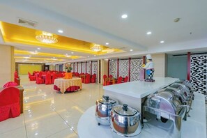 A banquet hall with round tables, chairs, and a buffet area with food containers.