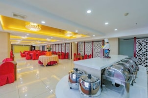 Un salón de banquetes con mesas redondas, sillas y una zona de bufé con recipientes de comida.