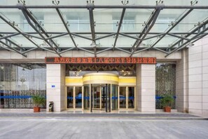 A hotel entrance with a glass canopy, a revolving door, and a sign above the entrance. - Hua Tian Hotel (Tianshui)