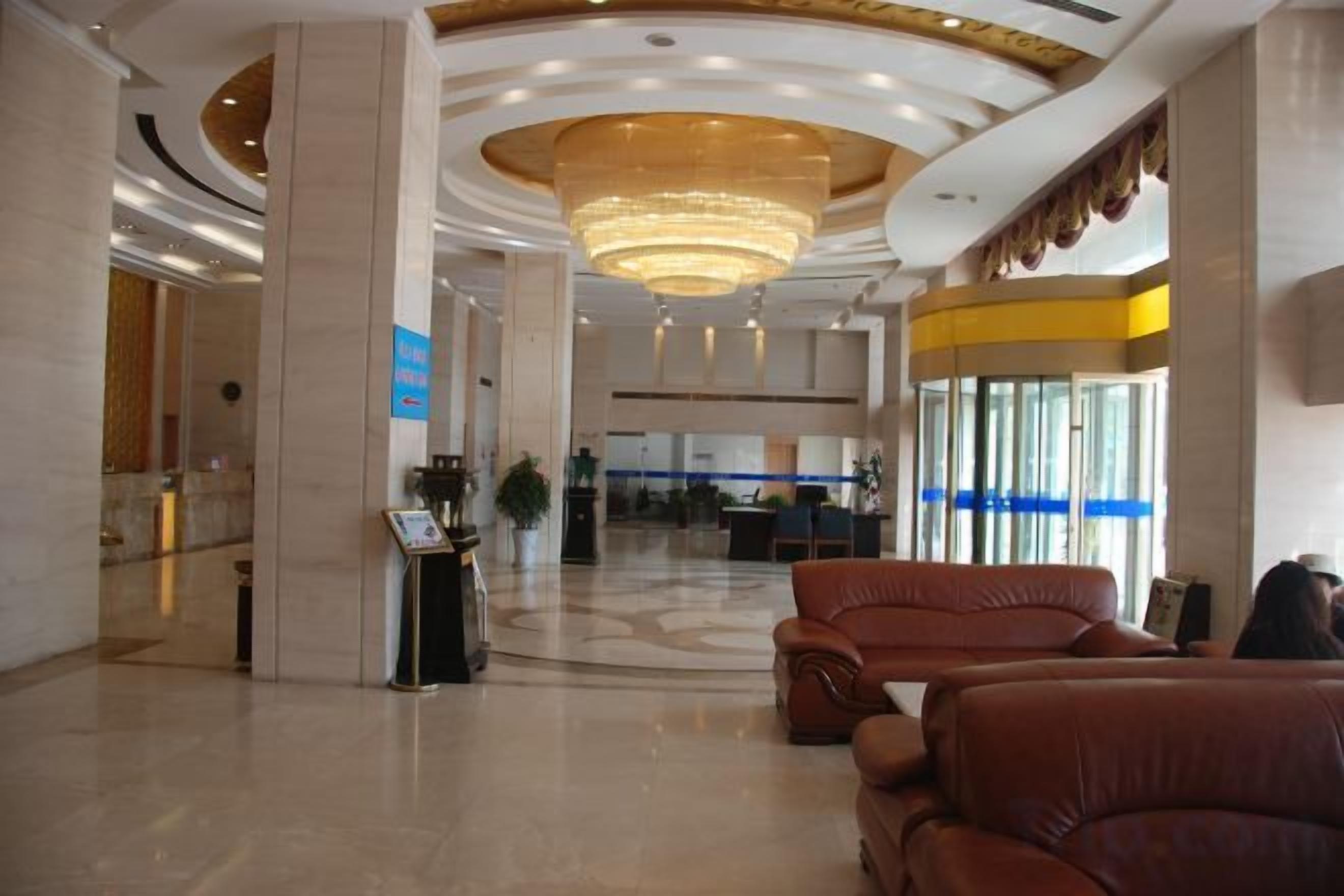 A hotel lobby with a reception desk, seating area, and a large chandelier.