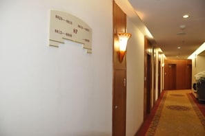 A hotel hallway with a carpeted floor, wooden doors, and a wall-mounted sign with room numbers. - Hua Tian Hotel (Tianshui)