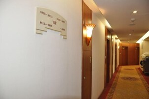 Un pasillo de hotel con piso alfombrado, puertas de madera y un letrero en la pared con números de habitaciones.