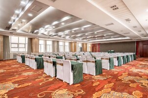 Un salón de conferencias con filas de mesas y sillas, ventanas amplias y una alfombra estampada.