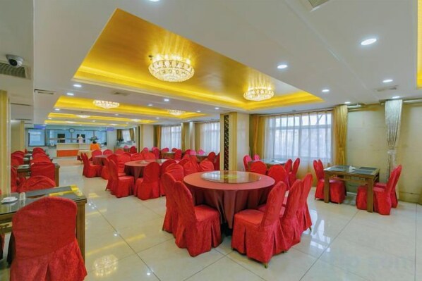 A banquet hall with round tables and chairs, a reception area, and chandeliers.