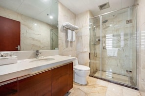 A modern bathroom with a marble vanity, a glass shower enclosure, and a toilet.