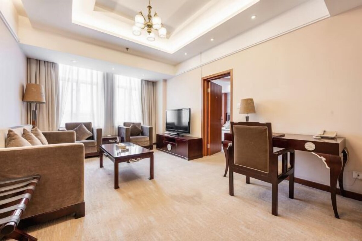 Habitación de hotel con sala de estar que incluye un sofá, una mesa de centro, un televisor y un escritorio con una silla.