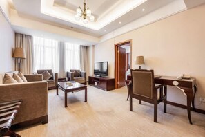 A hotel room with a living area featuring a sofa, a coffee table, a TV, and a desk with a chair. - Hua Tian Hotel (Tianshui)