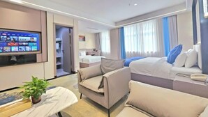 A modern hotel room with a flat-screen TV, a sofa, a bed with blue pillows, and a small table with a plant. - Hua Tian Hotel (Tianshui)