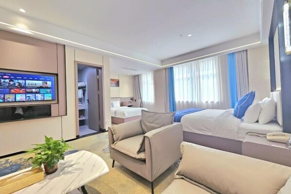 A modern hotel room with a flat-screen TV, a sofa, a bed with blue pillows, and a small table with a plant. - Hua Tian Hotel (Tianshui)