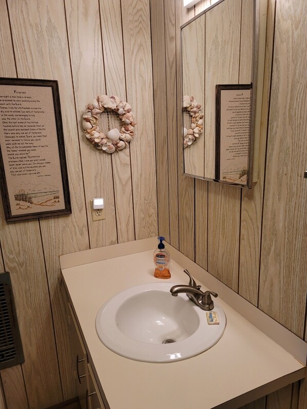 A bathroom with a wooden panel wall, a white sink with a soap dispenser, and framed quotes on the wall.