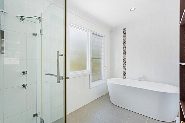 Ein modernes Badezimmer mit einer Glasdusche, einer freistehenden Badewanne und einem Fenster für natürliches Licht.