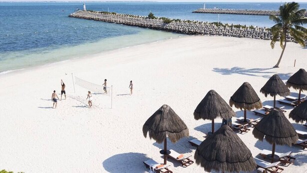 A beach with white sand, thatched umbrellas, and lounge chairs. - LA AMADA CANCUN LUXURY CONDO 3 BR STEPS FROM BEACH MARINA (Isla Mujeres)