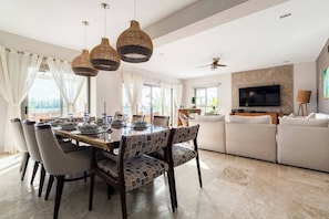 A modern living room with a dining area, featuring a large TV, comfortable seating, and a ceiling fan.