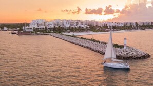 A sailboat on calm waters with a marina and white buildings in the background. - LA AMADA CANCUN LUXURY CONDO 3 BR STEPS FROM BEACH MARINA (Isla Mujeres)