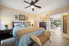 A bedroom with a large bed, bedside tables, a ceiling fan, and a view to the outside.