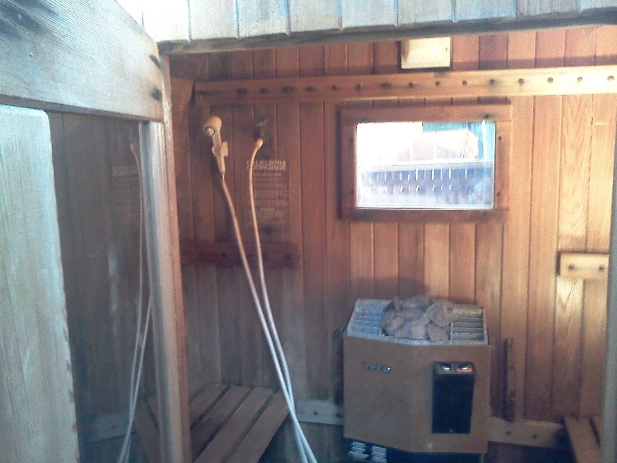 A sauna room with wooden walls, a window, and a sauna heater.