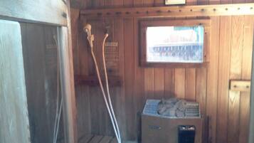 A sauna room with wooden walls, a window, and a sauna heater.