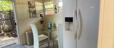 A compact kitchen with a white refrigerator, a small dining table with chairs, and a window providing natural light.