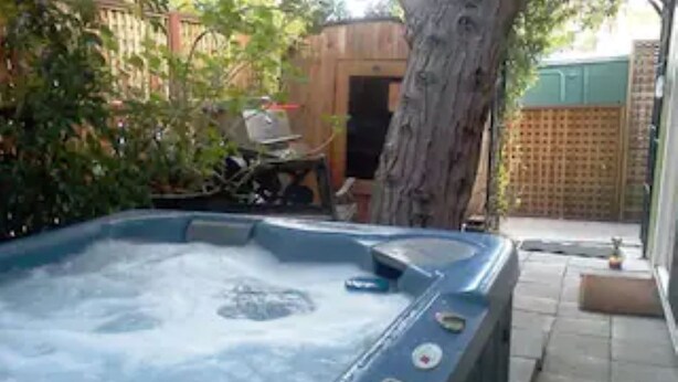 Een bubbelbad in een achtertuin met een houten omheining, een boom en een terras.