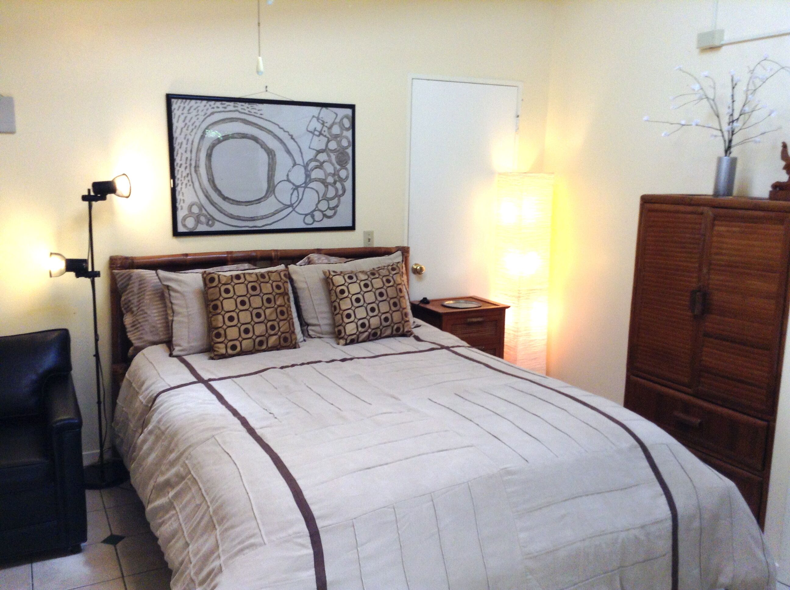 A bedroom with a bed, a nightstand, a lamp, a dresser, and a framed artwork on the wall.