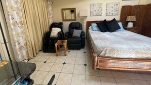 Een slaapkamer met een bed, een stoel, een bijzettafeltje, een spiegel en kunst aan de muur.