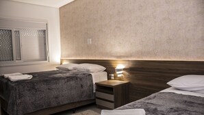 Habitación de hotel con dos camas, una mesita de noche, una lámpara de pared y una ventana con persianas.