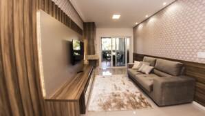 Una sala de estar moderna con televisor de pantalla plana, un banco de madera, un tapete estampado y un sofá gris.