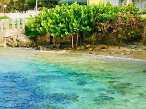 A beach with clear turquoise water, a stone wall, and lush greenery. - Sea Palms, Tower Isle: near Ocho Rios (Tower Isle)