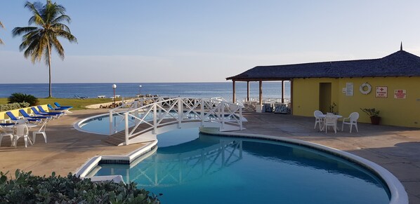 A pool area with a bridge, lounge chairs, and a building with a yellow facade. - Sea Palms, Tower Isle: near Ocho Rios (Tower Isle)
