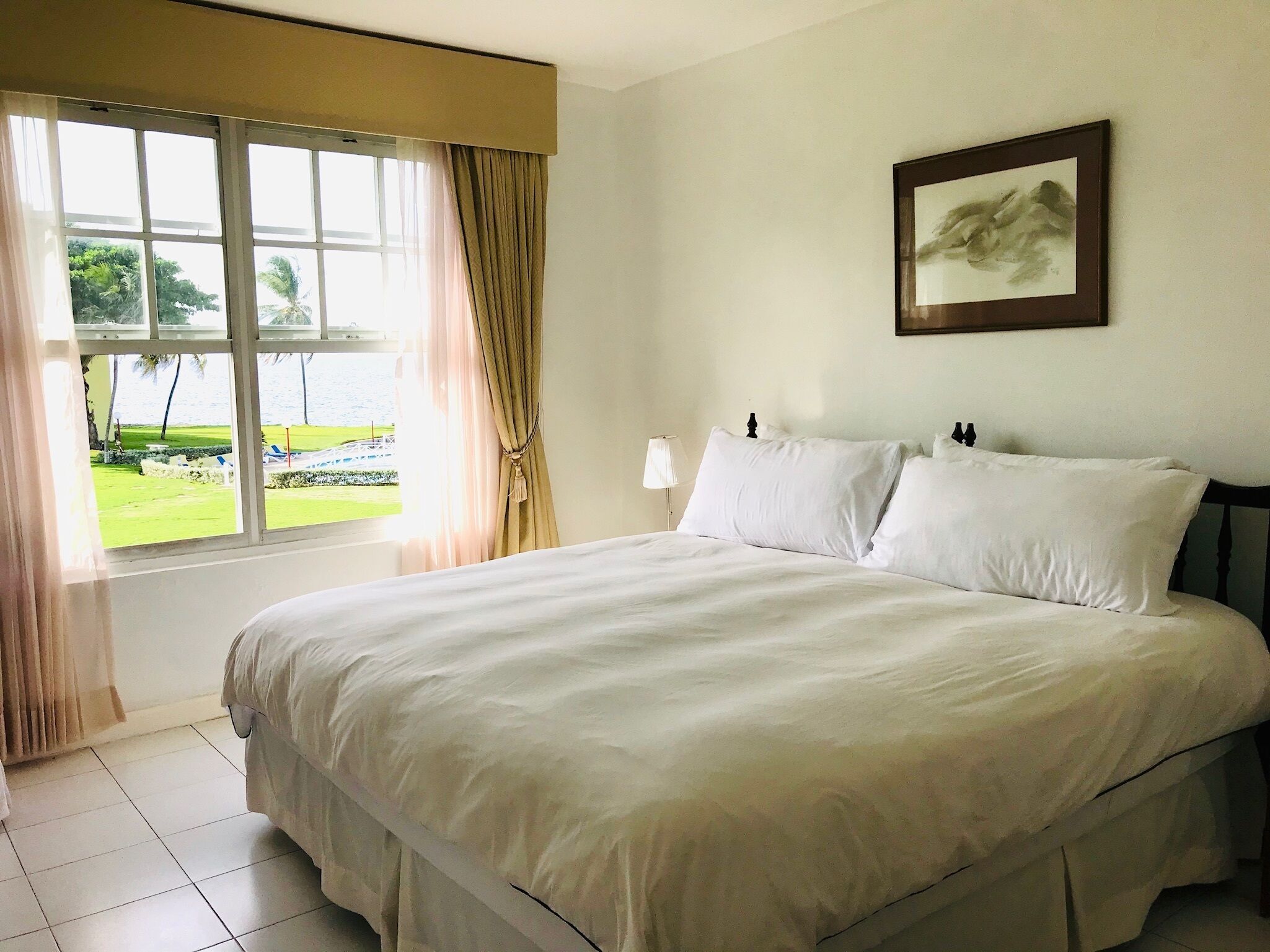 A hotel room with a large bed, a window with curtains, a bedside lamp, and a framed picture on the wall.