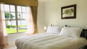 Habitación de hotel con una cama grande, una ventana con cortinas, una lámpara de noche y un cuadro enmarcado en la pared.