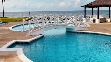 A swimming pool with a bridge, lounge chairs, and a gazebo.