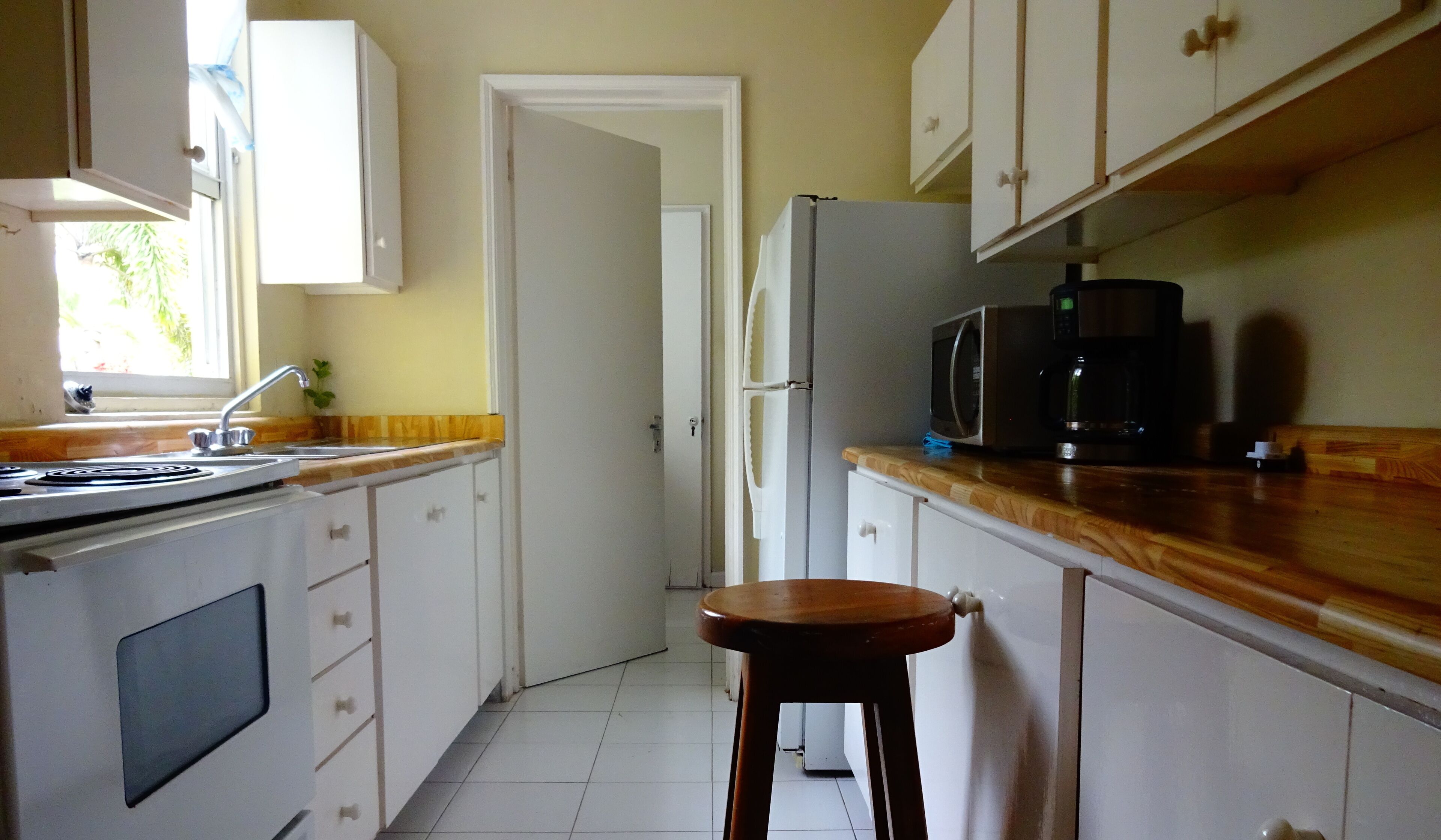 Una cocina con armarios blancos, estufa, fregadero, microondas y refrigerador.