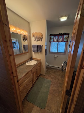 Ein Badezimmer mit einem Holzkosmetikschrank, einem großen Spiegel, einer Toilette und einem Fenster mit Vorhängen.