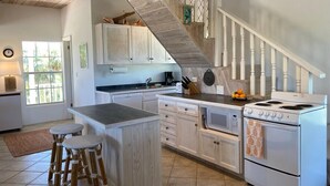 Una cocina con armarios blancos, una isla de madera con taburetes, una estufa y una escalera.