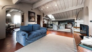 Un loft spacieux avec un plafond haut, des poutres apparentes, un canapé bleu à motifs et un coin cuisine.