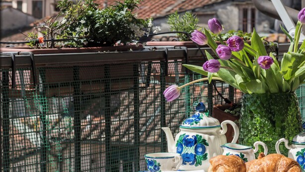 Une table recouverte d’une nappe blanche, un croissant, une théière et un vase rempli de fleurs.