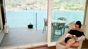 A woman sitting on a chair by a large window overlooking a body of water and hills. - Como Executive penthouse- 180 degree panoramic lake views by Italian Apartments. (Como)