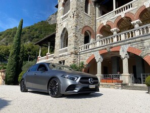 A luxury car parked in front of a historic stone building with arched windows and a balcony. - Como Executive penthouse- 180 degree panoramic lake views by Italian Apartments. (Como)