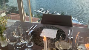 A dining table set with wine glasses and a candle, overlooking a lake with boats and buildings in the background. - Como Executive penthouse- 180 degree panoramic lake views by Italian Apartments. (Como)