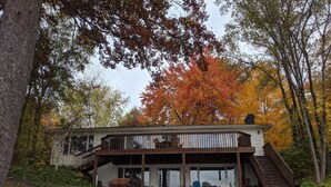 Una casa a due piani con un balcone, circondata da alberi con foglie autunnali.