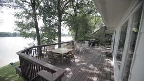 Un terrazzo in legno con tavolo e sedie, con vista su un lago.