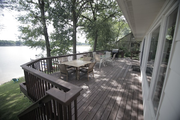 A wooden deck with a table and chairs, overlooking a lake.