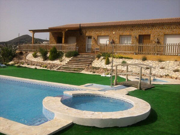 A pool area with a stone house in the background. - Rural lodging Los Castros (Bédar)