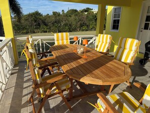 A wooden table with chairs, a glass with nuts, and a view of trees and a house.
