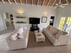 A living room with two beige sofas, a coffee table, a TV, and a ceiling fan. - Quiet Villa Near Beaches, Restaurants (West Indies)