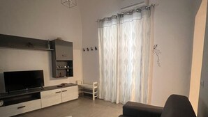 A modern living room with a flat-screen TV, a sofa, a coffee table, and a dining area with a cabinet and a microwave. - APARTMENT, VACATION HOME CATANIA (Catania)