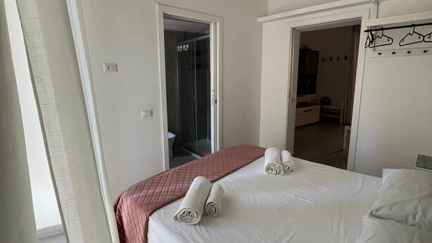 A hotel room with a bed, a door leading to a bathroom, and a coat rack with hangers. - APARTMENT, VACATION HOME CATANIA (Catania)