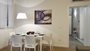 A dining area with a table set for four, white chairs, a wall-mounted lamp, and a painting. - Rialto twins house, in the center of the city (Venezia)